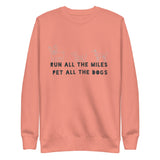 Image of the back of a peach sweatshirt , pictures of three cute dogs, says "Run all the miles, pet all the dogs"